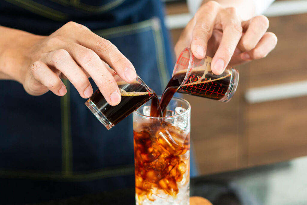 a person pouring a drink into a tall glass